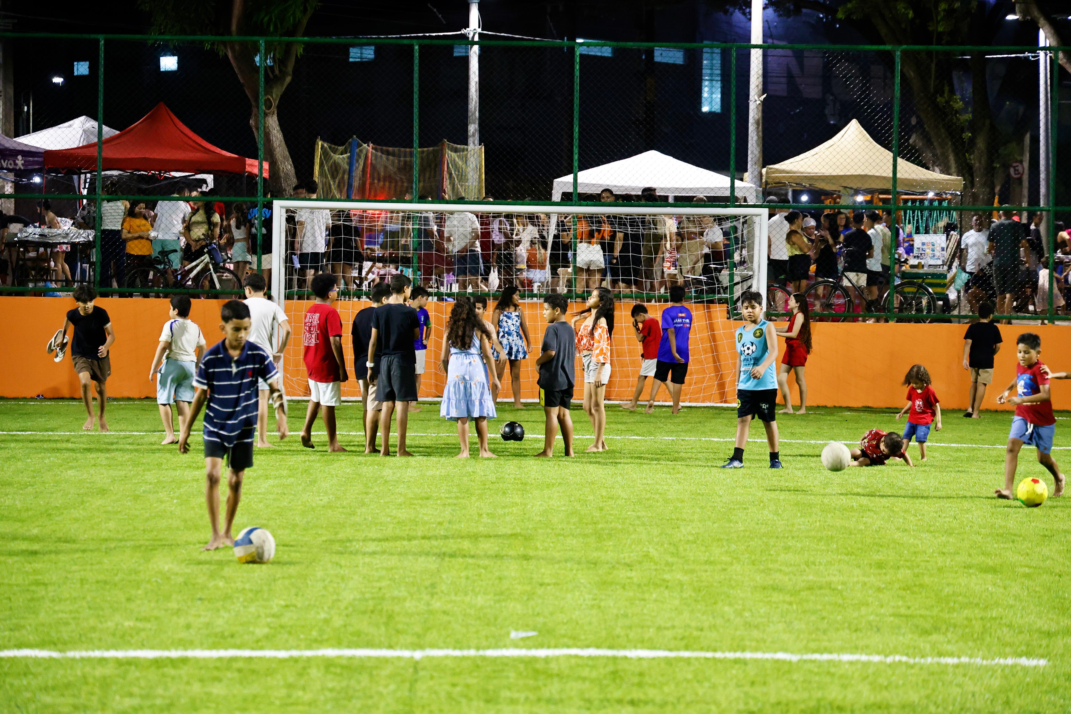 A foto mostra a areninha da Praça dos Encontros com diversas crianças jogando bola